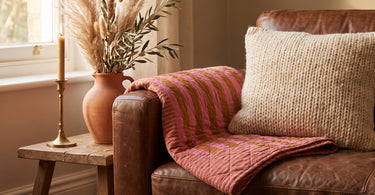 Quilt Ethnic plaid i pink og brun fra EJA på en brun lædersofa